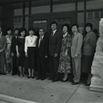 Ten people stand outside Chinatown Branch between two stone lions.