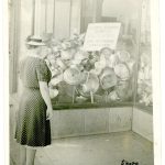 A woman stares into a storefront filled with pots and pans.