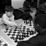 Boys play chess in black and white.