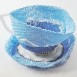 Teacup made of blue beads on a white and blue beaded saucer