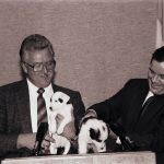 Two men at a podium with puppies