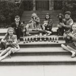 A group of children sit with their dogs surrounding trophies