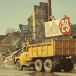 A yellow truck bearing the words "Bureau of Sewers" drives past a destroyed business and a sign advertising 29 cent suits