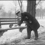 A man reaches out to touch a squirrel on a bench in the Boston Common in winter