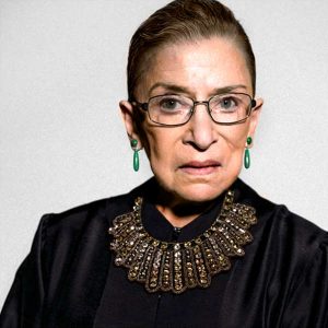 Image of Ruth Bader Ginsburg wearing her dissent jabot. It is gold with lines radiating from the top of the neckline to the bottom