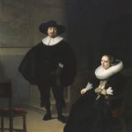 Man and woman dressed in black with white Elizabethan collars. The man is standing in the middle and the woman is seated to the right.