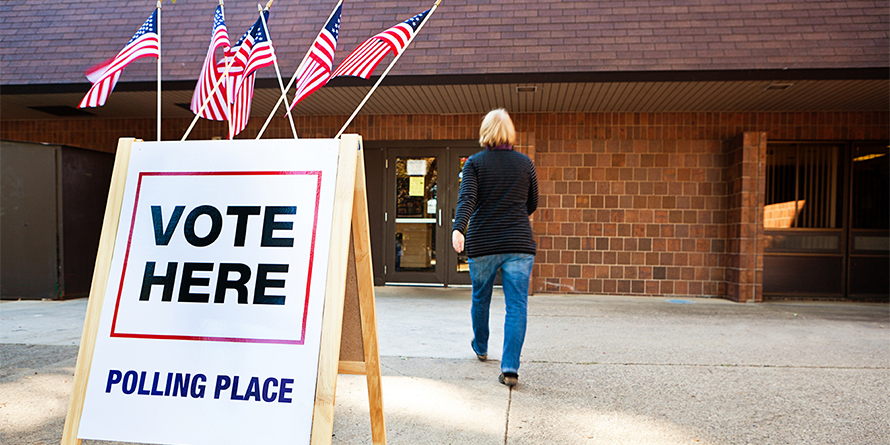 Unidentifiable woman voter entering a voting polling place for USA government election. Rear view shows her walking briskly in blurred motion by a sign decorated with American flags. For concepts of one person one vote, voter registration, voting booths, presidential and legistlative national and local decisions, democracy, and civic responsibility.
