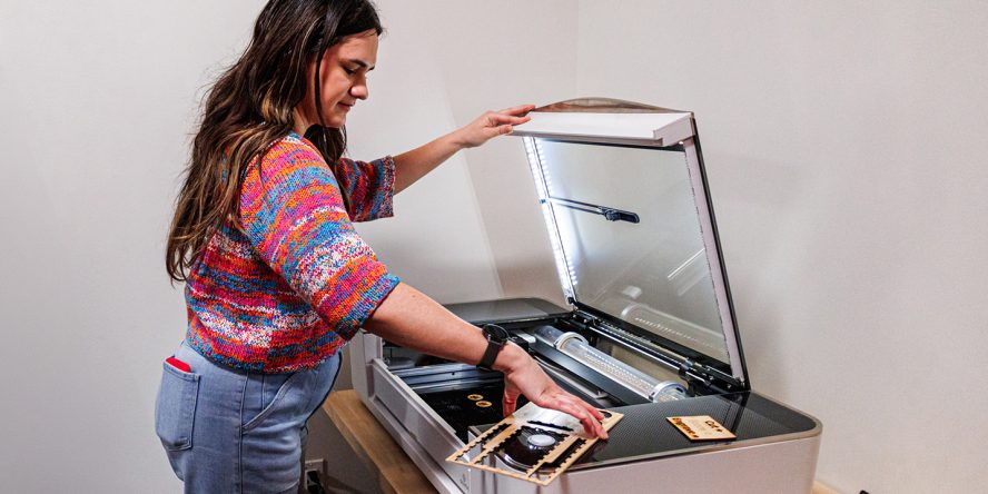 A woman with a colorful sweater operates a large laser cutter.