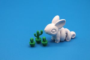 A small white figurine animal next to three miniature green cactus figurines against a blue backdrop.