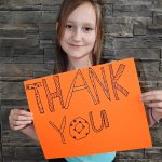 young girl holds up thank you card