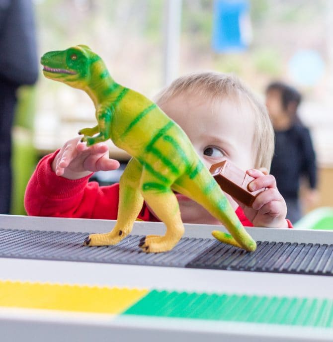 Child plays with dinosaur on a Lego table