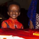 A young boy dressed as Spiderman grins at the camera from behind a table.
