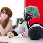 Two young people wearing masks sit at a table and look off camera at a Pokémon event at Halifax Central Library