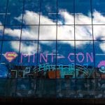 The Front Windows of the Second Floor at Halifax Central Library decorated with post-it notes to read: MINI-CON, May 9-14 along with a Superman logo and Pokémon Ball. Clouds are shining in the reflection of the windows.