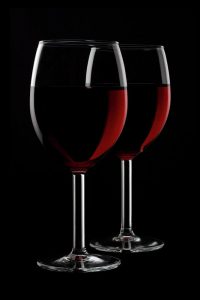 Image is of two glasses of red wine with a dark background