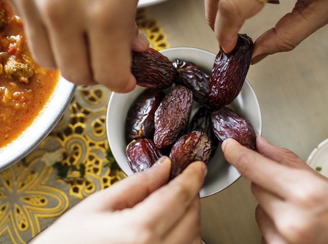 bowl of dates with hands reaching and grabbing fruit
