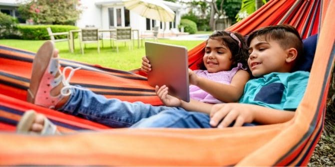 latinx boy and girl children kids reading on a tablet lying in a hammock