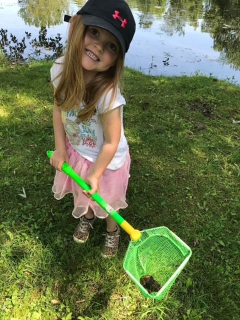 Girl holding small net with frog in it that she caught.