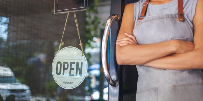 Woman stands next to open sign in doorway, small business reference center
