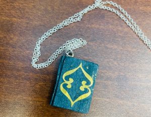 Blue-ish miniature book with gold details attached to a silver chain